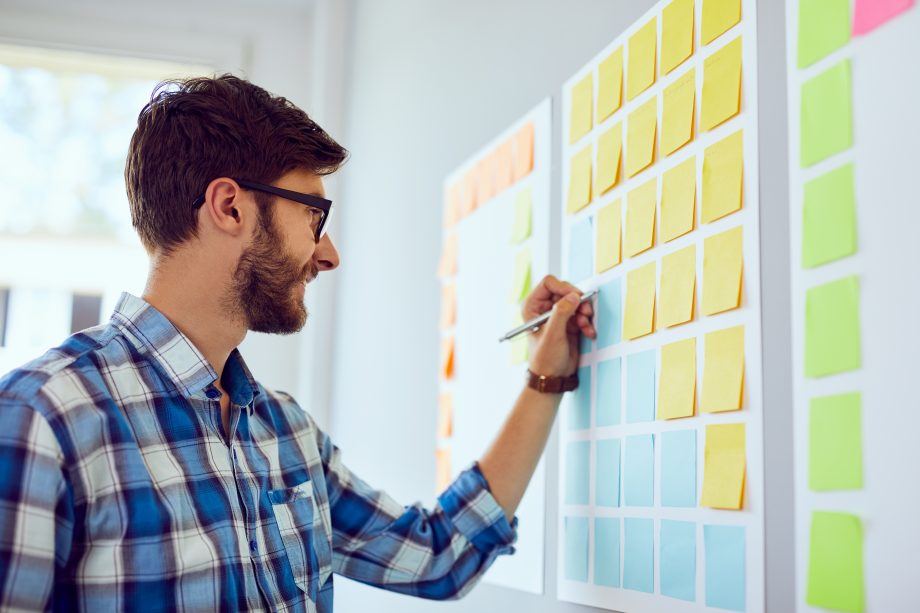 Young creative designer working on startup business in his office, writing on sticky-notes on a whiteboard